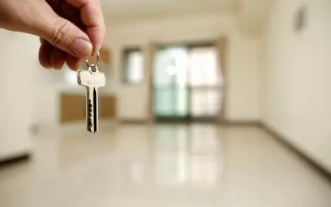Mano sosteniendo una llave plateada frente a una habitación vacía y desenfocada.
