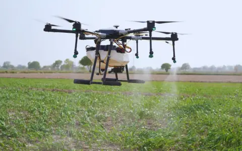 A drone sprayer, one of the types of drones in agriculture, hovers over a field, dispensing liquid onto crops.