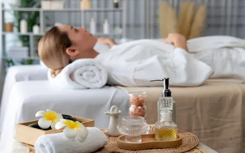 Relaks w jednym z hoteli spa Polska. Kobieta w białym szlafroku leży na łóżku, otoczona kosmetykami i kwiatami.