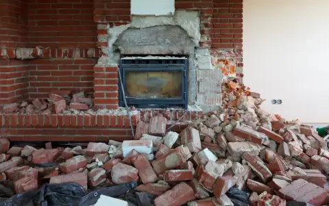 Démolition d'une cheminée en briques, laissant le conduit apparent. Des débris de briques jonchent le sol.