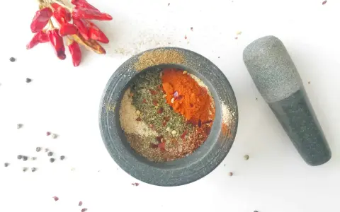 Mortier en pierre rempli d'épices pour fajitas, avec des piments rouges séchés et des grains de poivre à proximité.