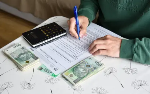 Osoba wypełnia dokumenty dotyczące umowy zlecenia i ubezpieczenia, obok leżą pieniądze i kalkulator.
