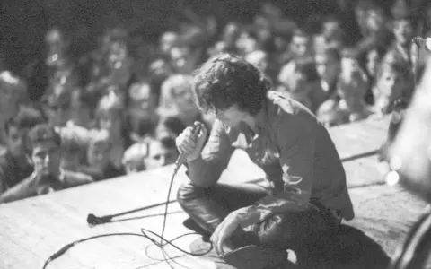 Jim Morrison z The Doors na scenie, wpatrzony w tłum. Jego "Paris Blues" rozbrzmiewa w sercach fanów.
