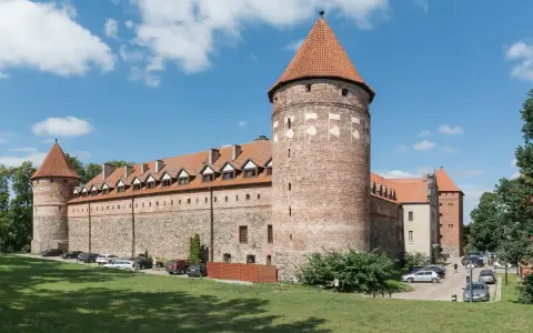 Bytów zamek krzyżacki, masywna budowla z cegły i kamienia z charakterystycznymi wieżami i czerwonymi dachami, otoczona zielenią.