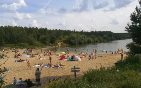 Tłoczna plaża nad jeziorem trzciańskim. Ludzie opalają się, kąpią i odpoczywają na piasku.
