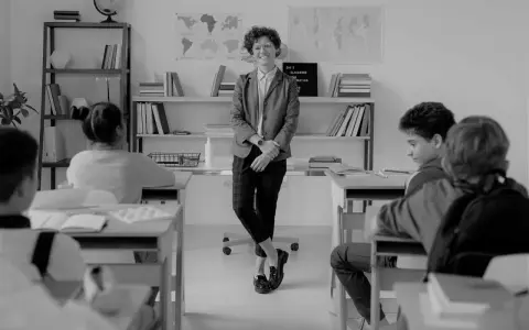 Lehrerin lächelt in einem Klassenzimmer, während Schüler an ihren Tischen sitzen. Eine Szene, die eine gute Klassengemeinschaft widerspiegelt.