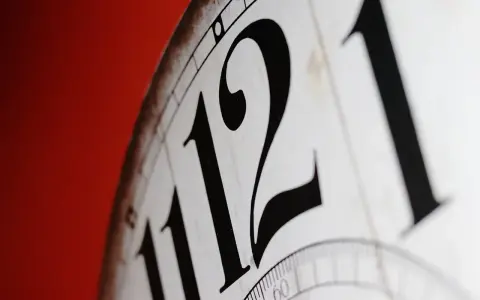 Zbliżenie na cyferblat zegara z dużymi, czarnymi cyframi 11 i 12. Nieważne, czy jest to am to rano czy wieczorem, czas płynie.