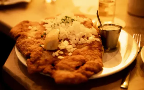 Ein knuspriges Schnitzel mit Zwiebeln und Zitrone, wie bei Oma Kleinmanns. Dazu ein Dip und ein Glas Wasser.