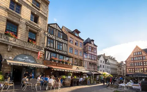 Terrasses animées devant les maisons à colombages de l'incontournable Rouen, sous un ciel bleu éclatant.