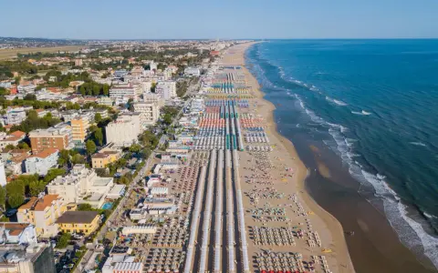 Vista aerea delle frazioni di Rimini: una lunga spiaggia attrezzata con file ordinate di ombrelloni e lettini, hotel e palazzi affacciati sul mare Adriatico.