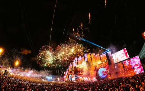 Feuerwerk über einer riesigen Menschenmenge bei Konzerten in Lissabon. Die Bühne ist mit Lichtern und Bildschirmen geschmückt, während die Menge jubelt.