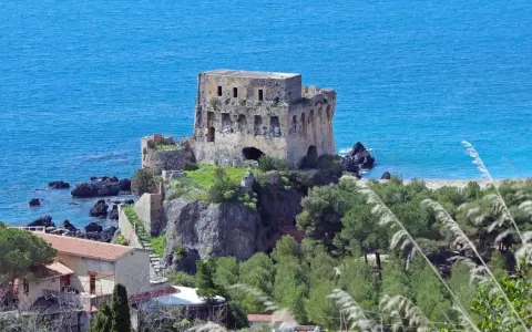 Torre aragonese a picco sul mare, uno dei borghi da visitare in Calabria, con case e vegetazione lussureggiante.