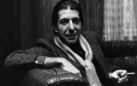 Leonard Cohen, mit Schal und Zigarette, sitzt nachdenklich auf einem Ledersofa. Ein ikonisches Bild, das den Geist des Sängers einfängt.