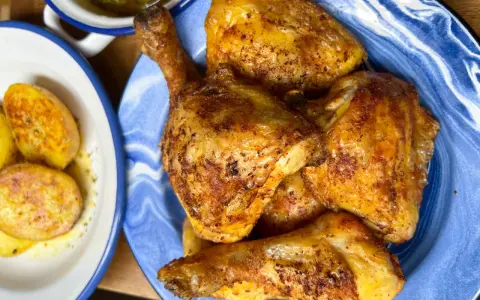 Pollo dorado y jugoso troceado en un plato azul, acompañado de patatas y pimientos.