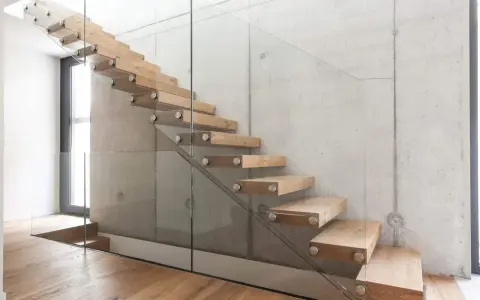 Moderne Holztreppe mit Glasgeländer an Betonwand. Hier können Sie die treppe kosten berechnen.