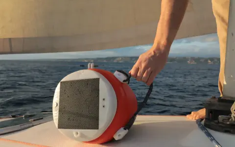 Main tenant une bouée orange et blanche, prêt à la mouiller à hauteur. La mer et le ciel bleu en arrière-plan.