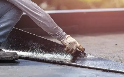 Hand mit Handschuh legt neue Dachpappe an. Alte Dachpappe entsorgen ist der nächste Schritt.