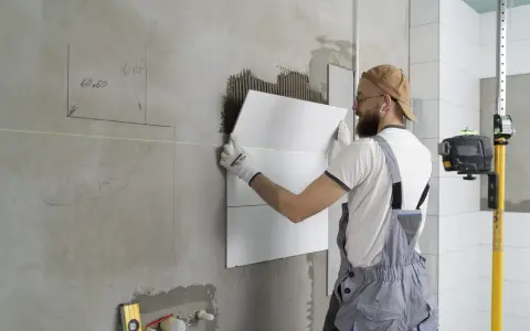 Obrero coloca baldosas en pared, usando nivel láser para asegurar un acabado perfecto. El proceso de instalación de aislante paredes interiores avanza.