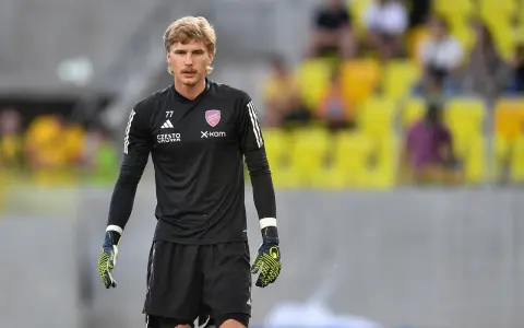 Mateusz Zych, bramkarz w czarnej koszulce z numerem 77, gotowy do akcji na boisku.
