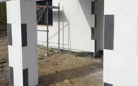 Budowa domu z bloczków styropianowych. Czy trzeba kołkować styropian grafitowy? Widok na fragment ściany i słupa z szarego styropianu.