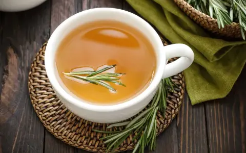 Une tasse d'infusion romarin dorée, garnie d'une branche de romarin frais, sur un dessous de plat en osier.