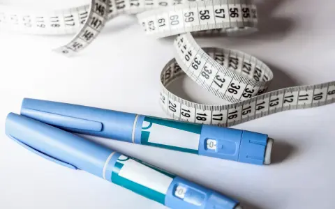 Dwa peny do iniekcji leków GLP-1 i miarka krawiecka symbolizują drogę do zdrowia i kontroli wagi.