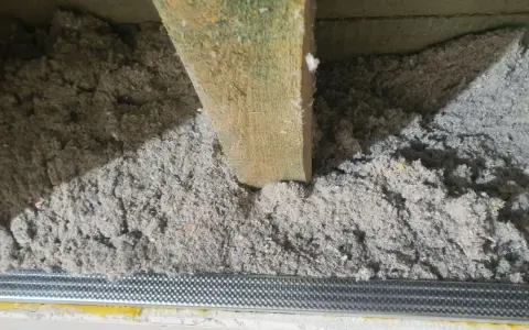 Izolacja z celulozy wypełnia przestrzeń między drewnianymi belkami stropowymi, tworząc warstwę termoizolacyjną.