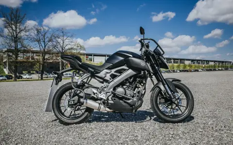 Czarny motocykl Yamaha, idealny na pierwsze prawo jazdy a1, stoi na żwirowym placu przed budynkiem.