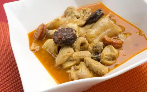 Un plato de callos a la madrileña con chorizo y morcilla en una cazuela blanca.