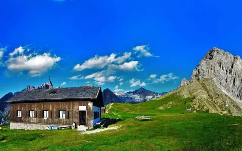Rifugio Passo San Nicolò, un'accogliente baita in legno con vista su maestose cime innevate e un cielo azzurro brillante.