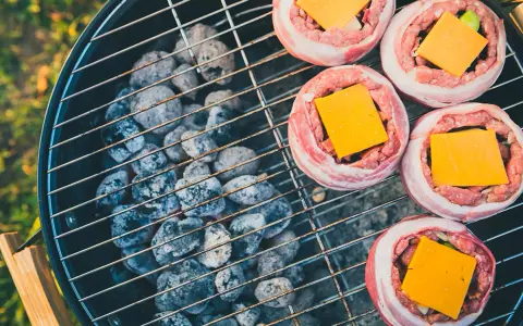 Fem baconsnurrade köttfärsbiffar med ost på en grill för indirekt grillning.