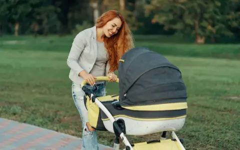 Uśmiechnięta mama z rudymi włosami pochyla się nad wózkiem. Idealny spacer, gdy zastanawiasz się, jak ubrać niemowlę 20 stopni.