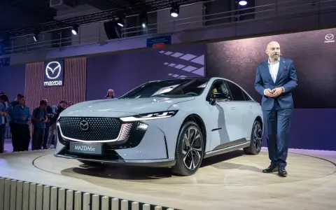 Elegancki, szary sedan Mazda6e prezentowany na scenie przez mężczyznę w garniturze.