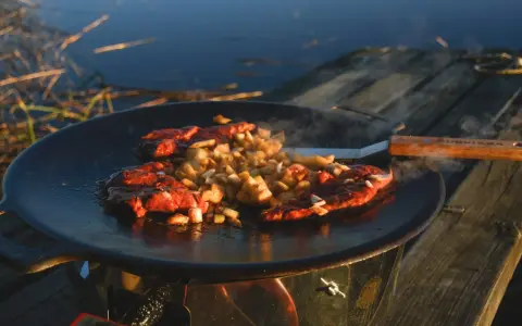 Kött och potatis steks på en rostig muurikka vid vattnet. En stekspade med trähandtag ligger bredvid.