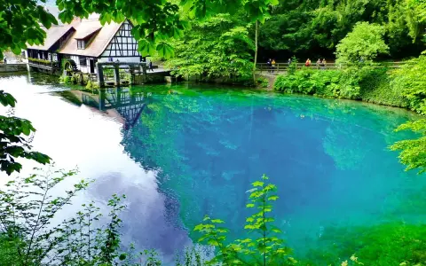 Der Blautopf See lädt zum Schwimmen ein. Ein historisches Fachwerkhaus mit Wasserrad spiegelt sich im kristallklaren, blauen Wasser.