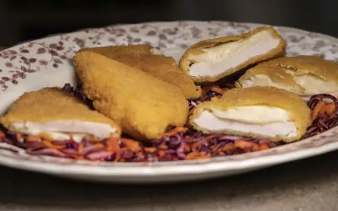 Pechuga villaroy dorada y crujiente, rellena de queso fundido, servida sobre una ensalada de col morada y zanahoria.