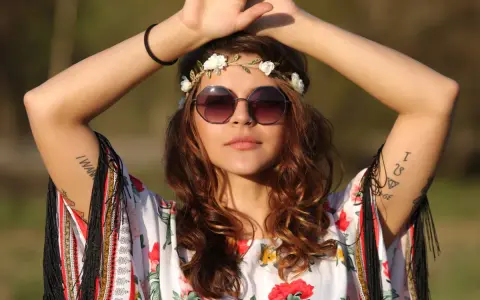 Dziewczyna w stylu boho, z wiankiem z kwiatów i okularami, w kwiecistej bluzce. Jej moda nawiązuje do wolności i natury, jak u dzieci kwiatów.