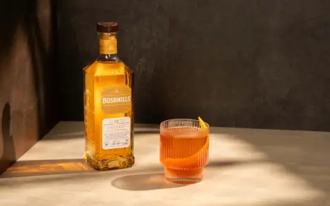 Butelka Bushmills 15 Year Old Single Malt Irish Whiskey obok szklanki z drinkiem. Wiele pozytywnych bushmills whisky opinie potwierdza jego wyjątkowy smak.