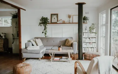 Przytulny salon w stylu skandynawskim nowoczesnym. Szara kanapa, drewniany stolik, regał z książkami i mnóstwo zieleni tworzą relaksującą atmosferę.