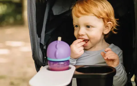 Rotschopf-Kind im Kinderwagen, isst genüsslich einen Snack. Dieses Kind hat immer Hunger und freut sich über jede Leckerei.