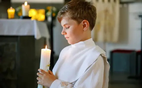 Chłopiec w białej szacie trzyma zapaloną świecę. To ważny moment, jak zorganizować chrzciny, by był niezapomniany.