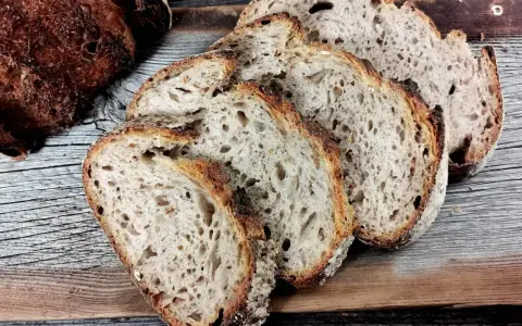 Ein Laib Sauerteigbrot, angeschnitten, mit sichtbarer, knuspriger Kruste. Die Scheiben zeigen eine luftige Krume. Hoffentlich ist die brotkruste zu hart, um sie zu genießen.