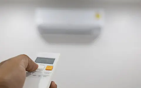 Mano che preme il telecomando per regolare il condizionatore. Il suo significato è comfort e controllo della temperatura.