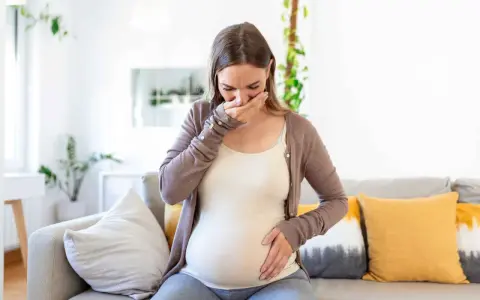 Donna incinta con nausea nel terzo trimestre, copre la bocca con la mano.