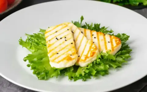 Grillowany ser halloumi na sałacie, posypany czarnuszką. Czy ser halloumi jest zdrowy? To pyszna przekąska.
