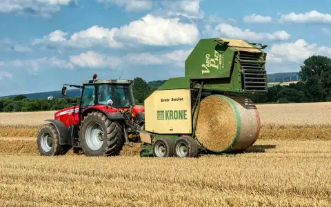 Czerwony traktor Massey Ferguson 6180 z prasą Krone Vario Pack na polu. Dane techniczne tej maszyny pozwalają na efektywne belowanie.