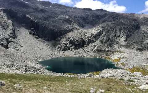 Ein tiefblauer Bergsee in der Sierra de Gredos, umgeben von felsigen Hängen und grünen Wiesen.