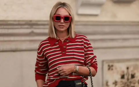 Donna con occhiali rossi oversize e maglione a righe rosse e bianche, un look che evoca un sofisticato preppy style.