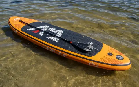 Pomarańczowy aquamarina sup z wiosłem leży na płytkiej, przejrzystej wodzie.