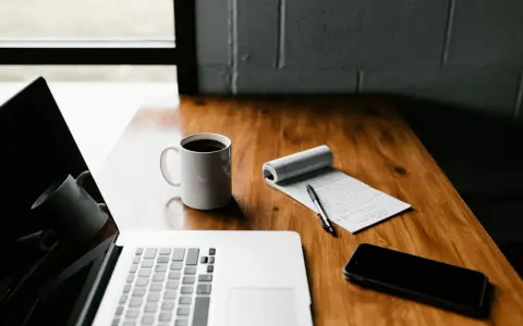 Laptop, kawa, notatnik i telefon na drewnianym biurku. Czas pomyśleć, jak zakonczyc bloga po ang.